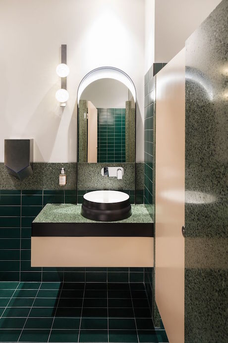 The bathrooms bring a surprising burst of color to the otherwise understated interiors with a playful palette of deep greens and apricots, softened by terrazzo partitions. Image courtesy of Daniel Shipp. 