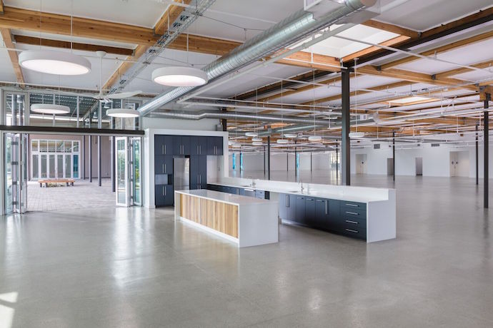 The design utilizes thermal mass and omits the need for an expensive T-Bar drop ceiling by exposing the wood beams and keeping the ceilings as high as possible. The ceiling is upholstered with reflective acoustical fabric, which reduces noise and spreads light more evenly throughout the space. Image courtesy of WRNS Studio. 